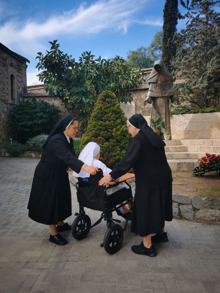 Madre Dulce es acercada en su silla por dos madres de la congregación a la escultura de M. Petra en la explanada del santuario.